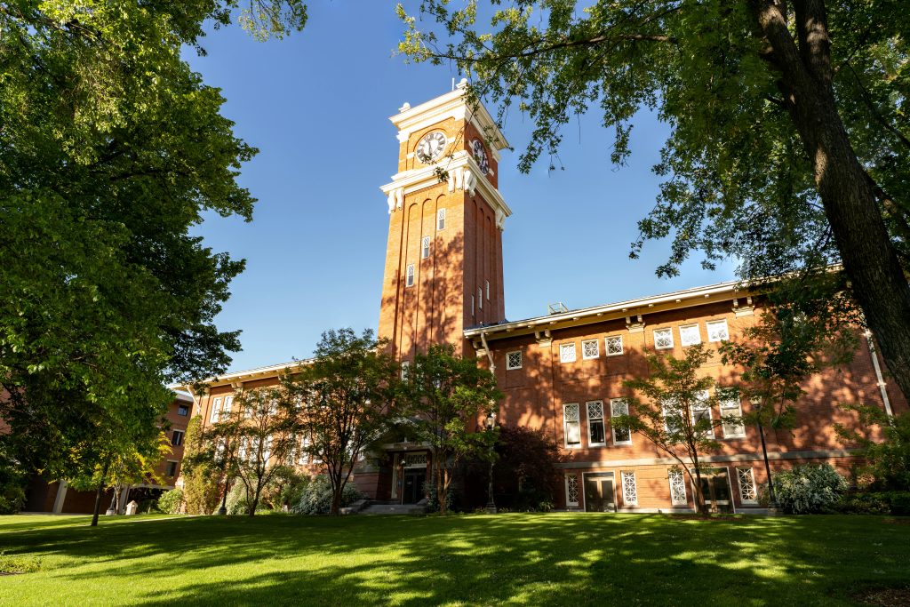 Beautiful view of the iconic clock tower at WSU under a clear blue sky, surrounded by lush greenery.