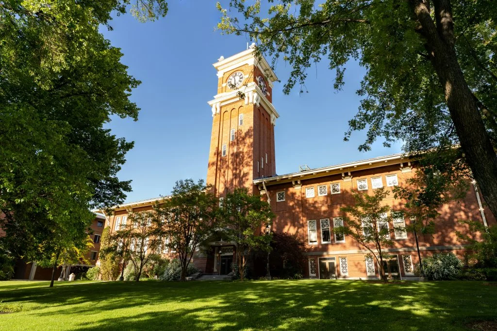 Beautiful view of the iconic clock tower at WSU under a clear blue sky, surrounded by lush greenery.